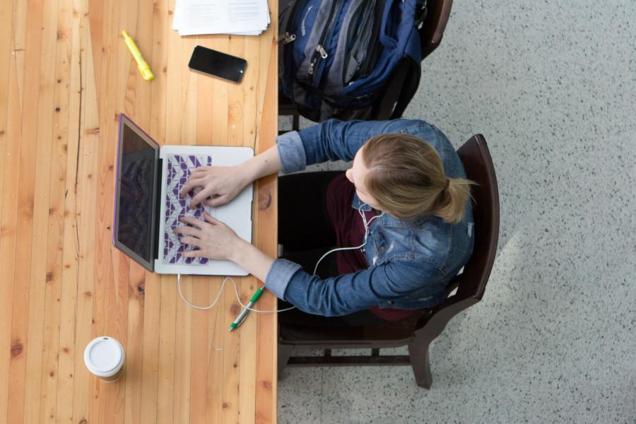 A student sits at a table working on a laptop.