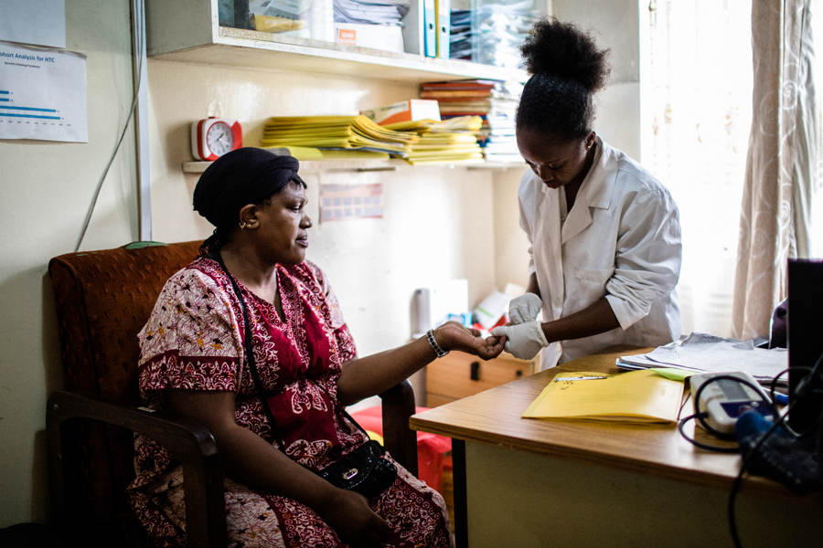 A woman in a lab coat holding the hand of a woman seated on a chair. 