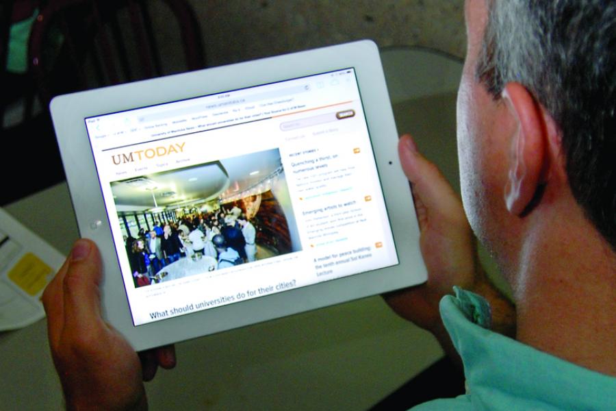 Image of a person holding a tablet, looking at the UM Today news site.