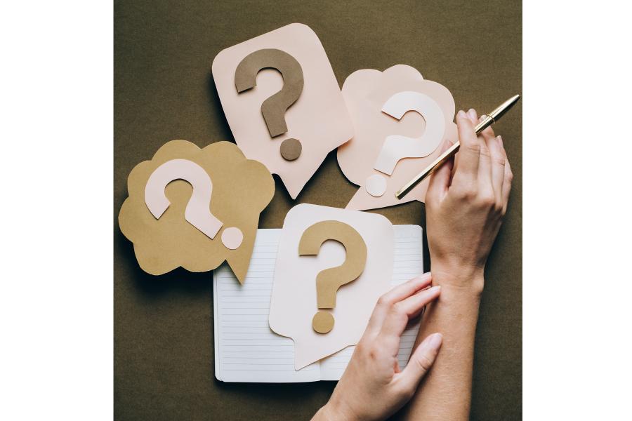 An image of questions marks and a hand holding a pen.