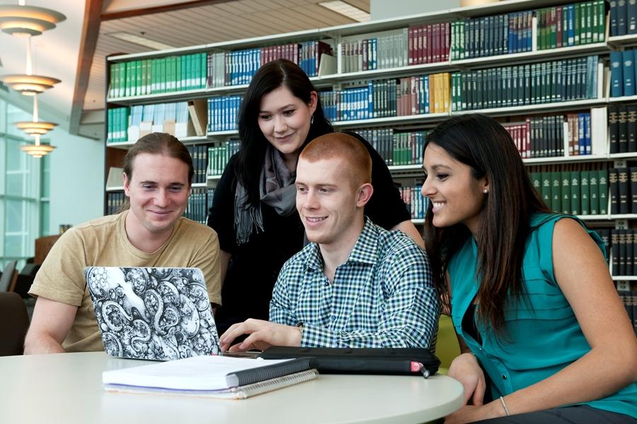 Group of four students look at a laptop screen, smiling.