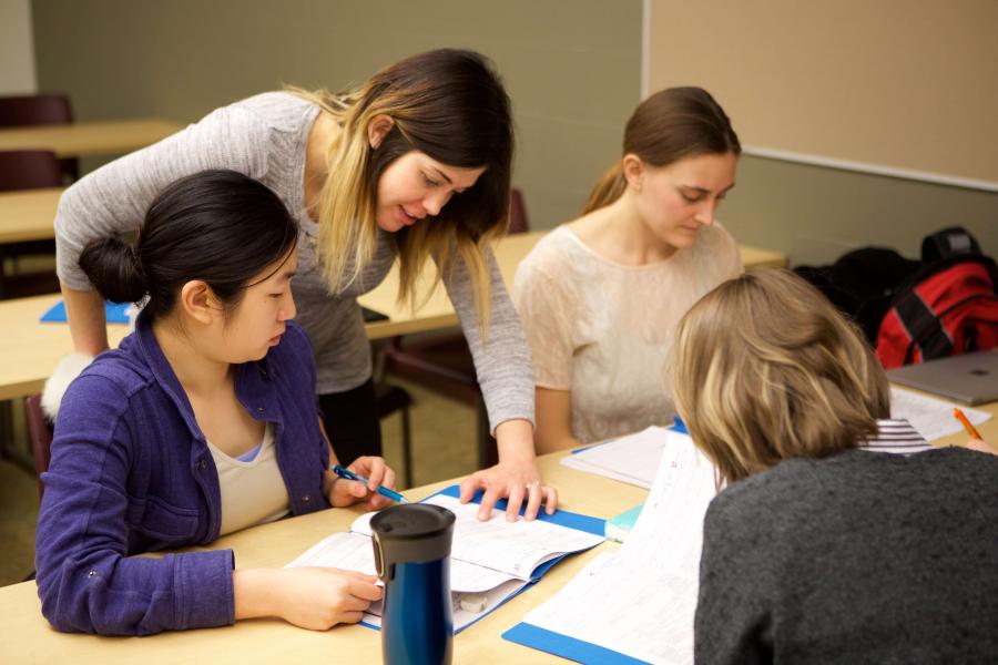 Students with a teacher looking over their shoulders at a desk.