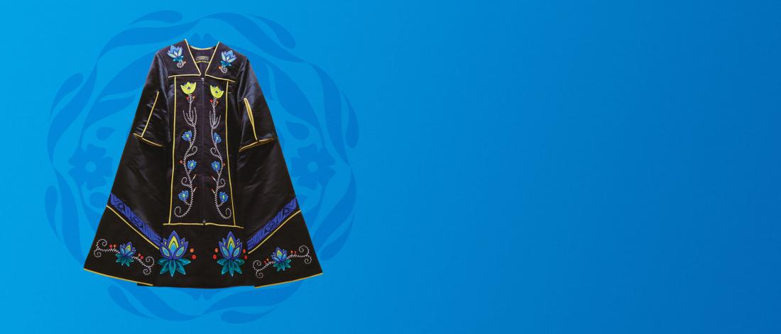 A black convocation gown with embroidery by an Indigenous artist against a blue background