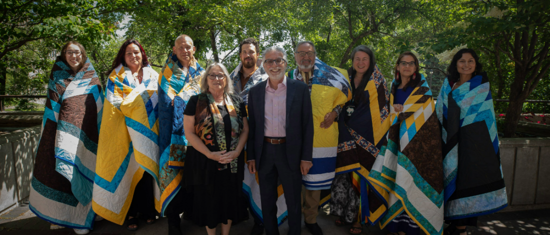 A group of Indigenous honourees standing outside wearing star blankets with the president and vice-president (Indigenous)