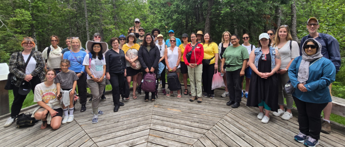 Group of program participants standing together on a wooden boardwalk in a forest during a land-based learning outing.