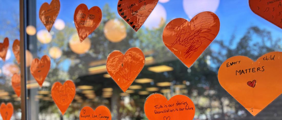 Orange paper hearts with messages for truth and Reconciliation are displayed on a window.