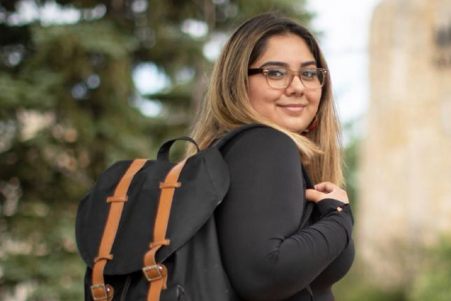 Female student wearing a black backpack looks over her shoulder with a smile.