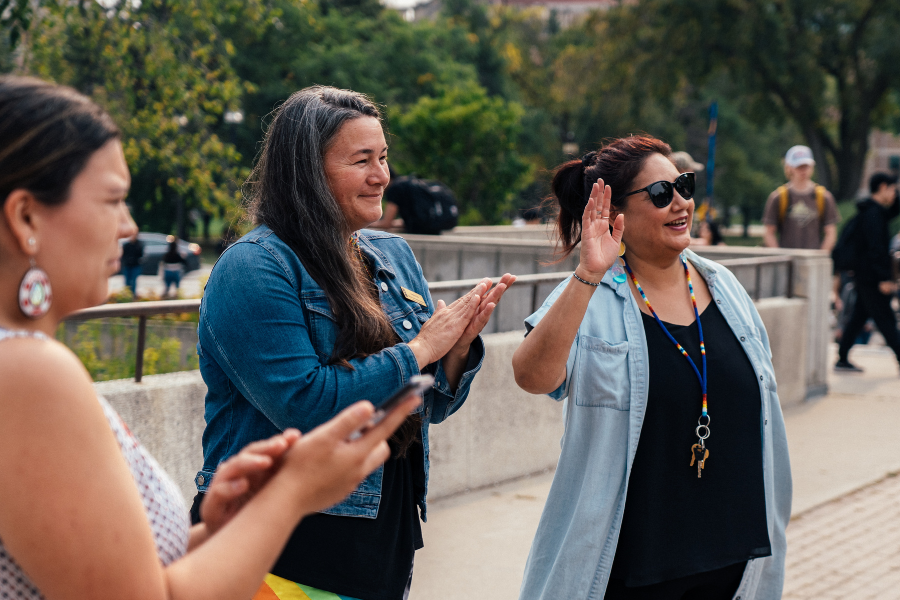  Three women standing outdoors, one clapping and another waving, creating a cheerful and welcoming atmosphere.