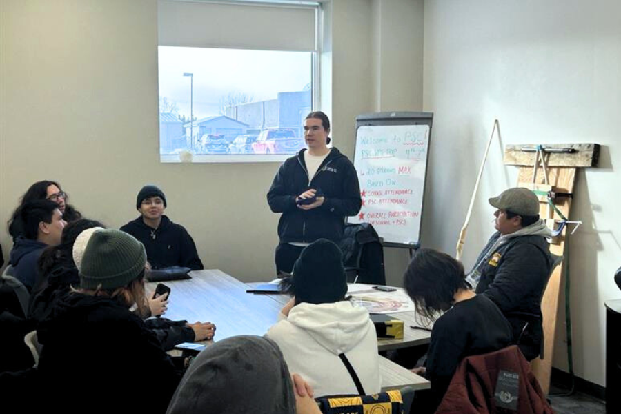 A student speaks to peers during an indoor workshop with a whiteboard in the background.