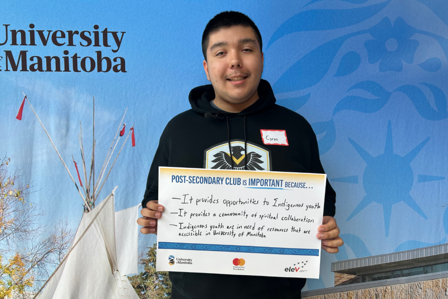  Student participant holding a sign sharing why the Post-Secondary Club is important, standing in front of a UM backdrop.