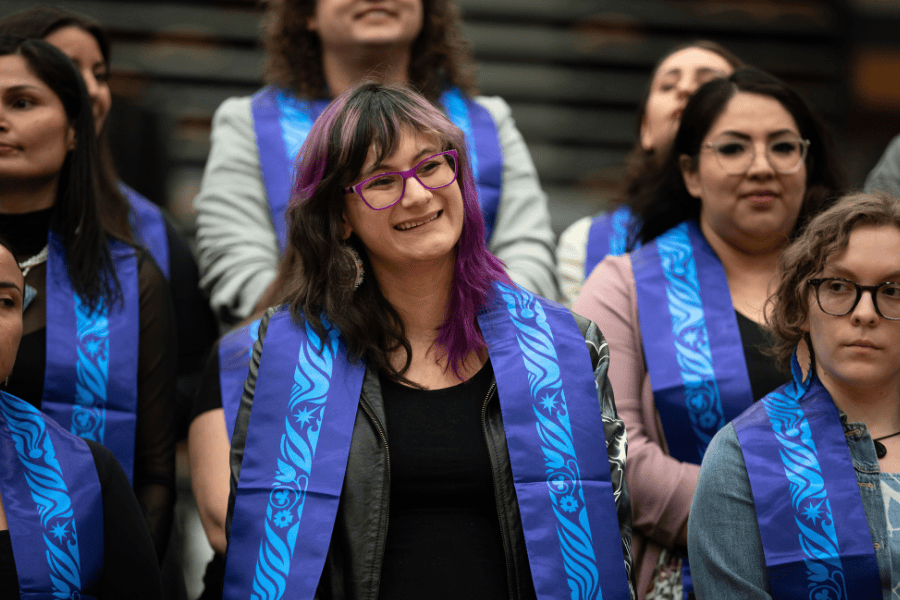 Indigenous graduate wearing a blue stole smiling during a pow wow ceremony