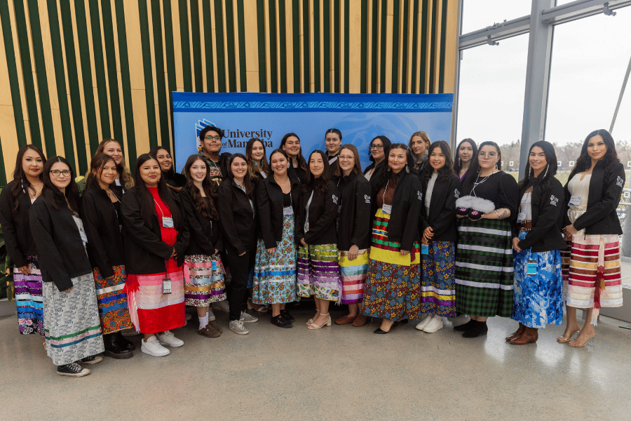 A group of Indigenous students stand in front of a backdrop.