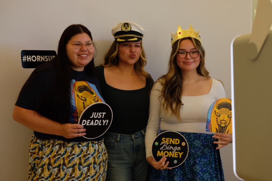 Three students posing with props at a photo booth.