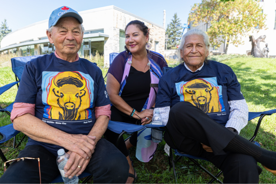 Three community members seated together outdoors and smiling.
