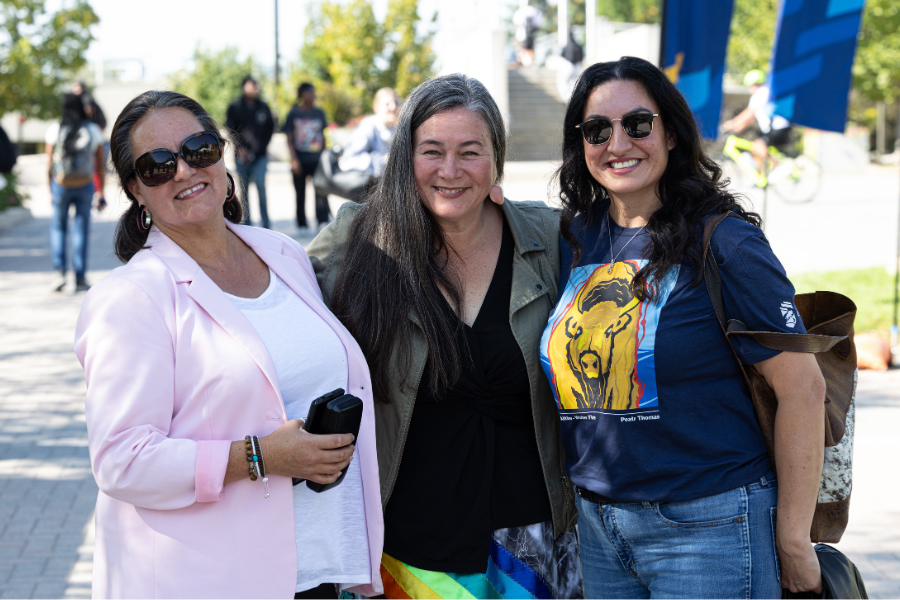 Three people smiling together at an outdoor campus event.