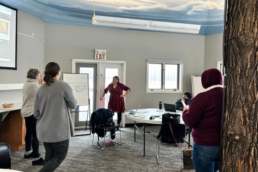 Participants gather in a meeting room, with one facilitator leading a group discussion while others listen, collaborate, and take notes.