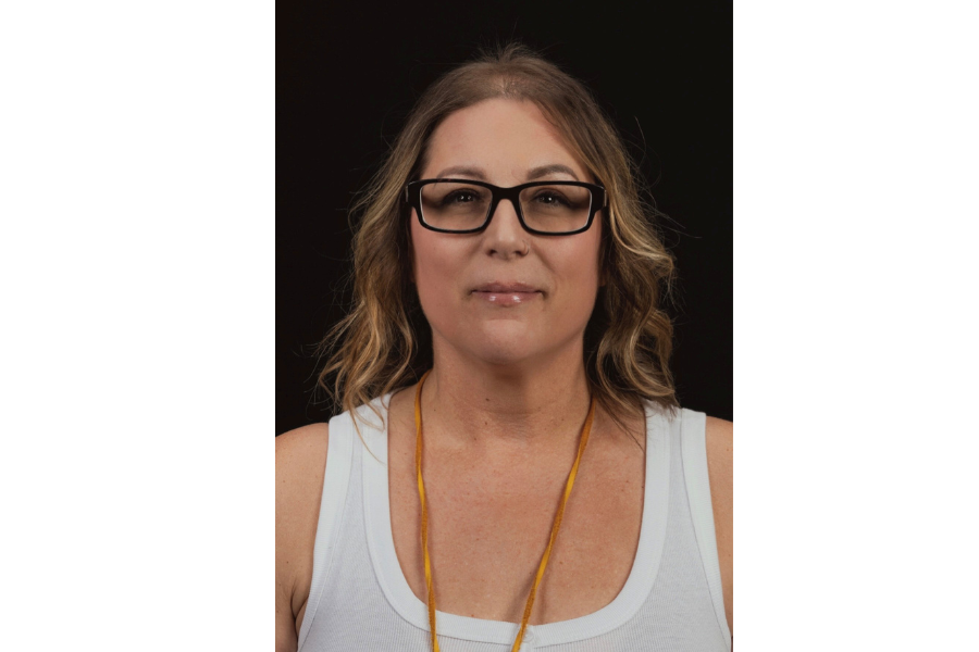 Headshot of Darcie wearing glasses and a white top against a black background.