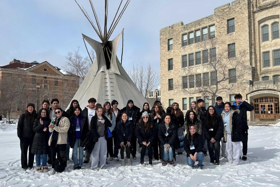 A group of students stand outside in the snow in front of a white tipi.