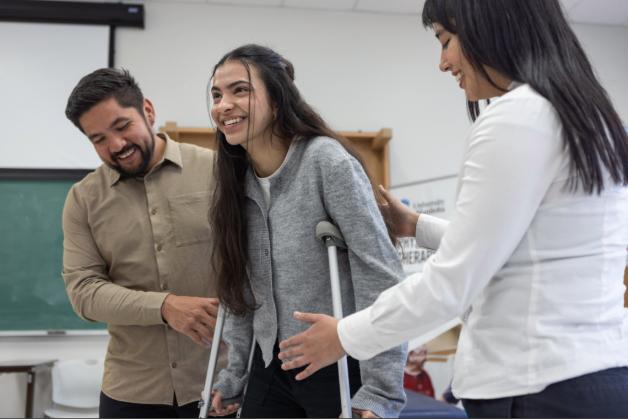 Two people helping a young girl walk on crutches