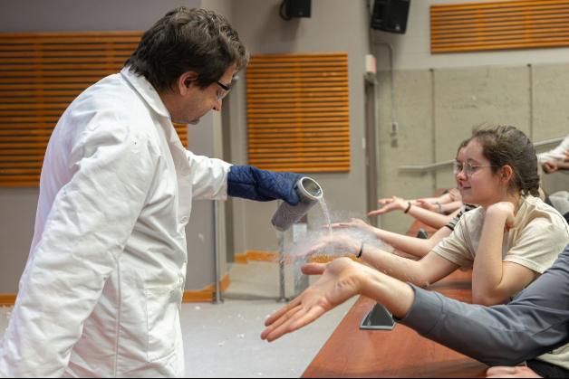 Man in lab coat pouring solution on hands of spectator