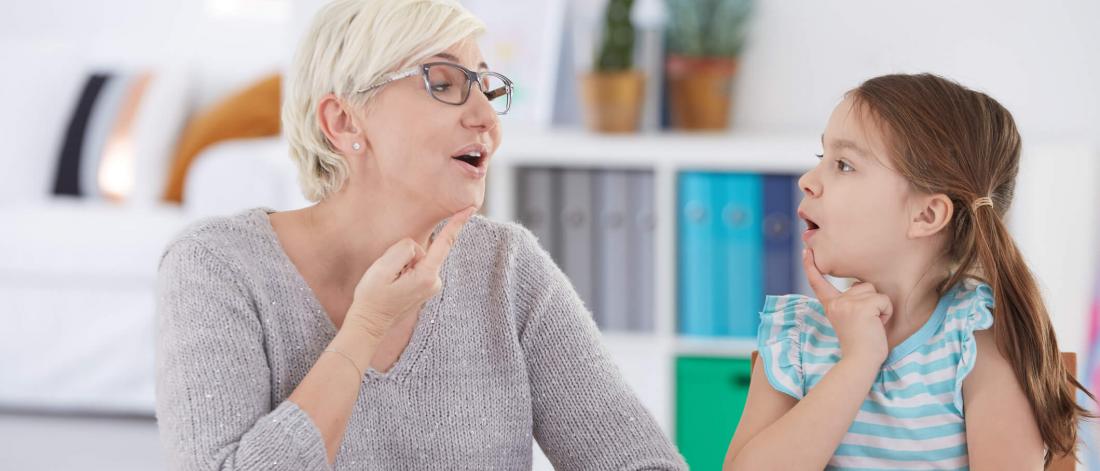 Therapist shows a child how to feel speech sounds by touching her throat.