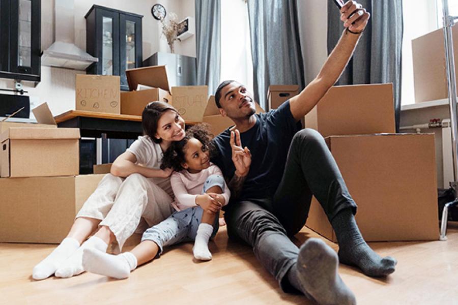 A couple taking a selfie with their daughter in a room filled with moving boxes.