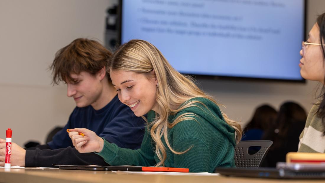 A femal UM student smiling at her work book as she discusses with a group