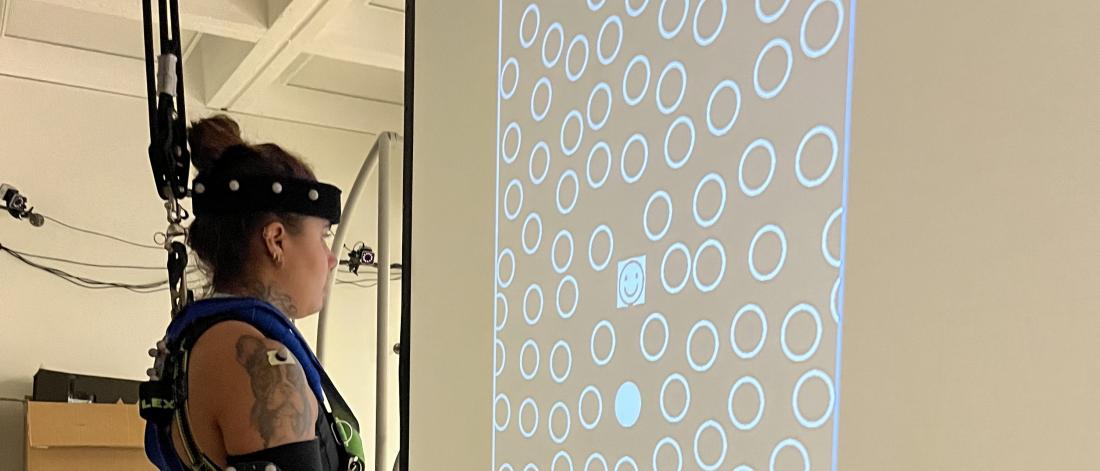 A woman standing in a harness viewing a screen with many circles on it during a lab test