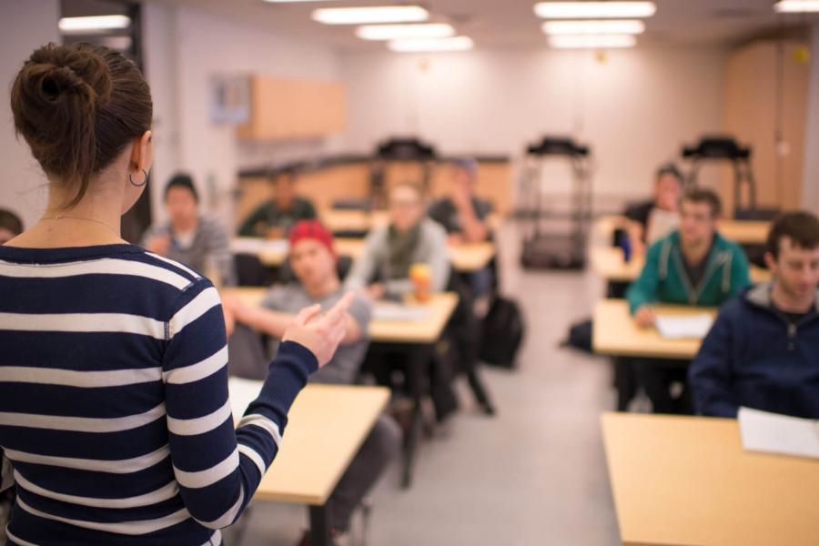 A teacher stands at the front of a classroom of listening students.