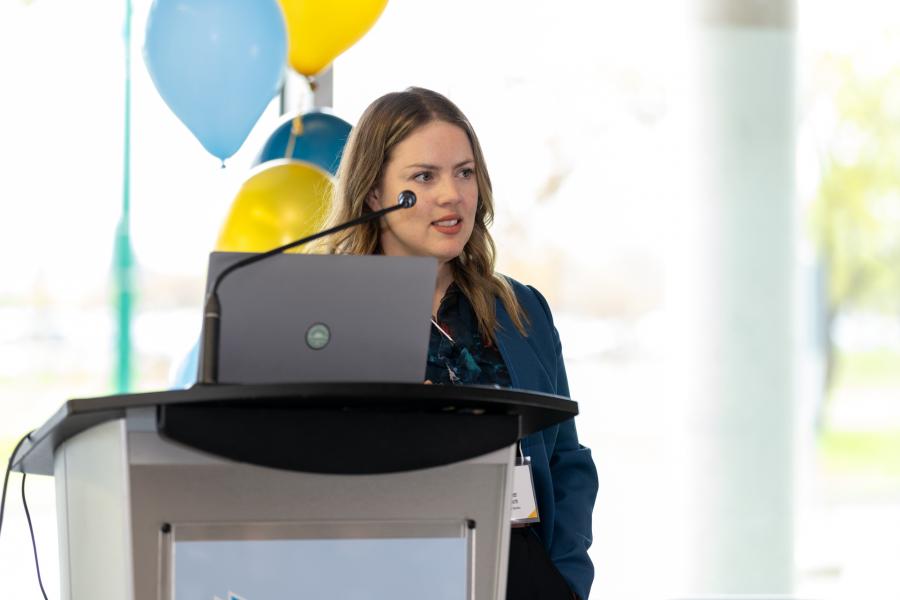 Dr. Heather Gainforth stands behind a lecturn and laptop while presenting