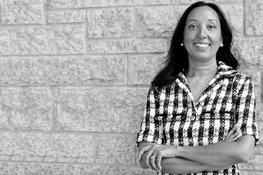 a woman in a black and white houndstooth shirt stands against a Tyndall stone brick wall