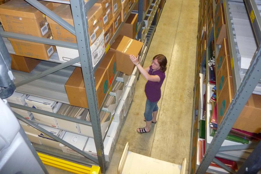 Woman removes box of archival records from a shelf full of records