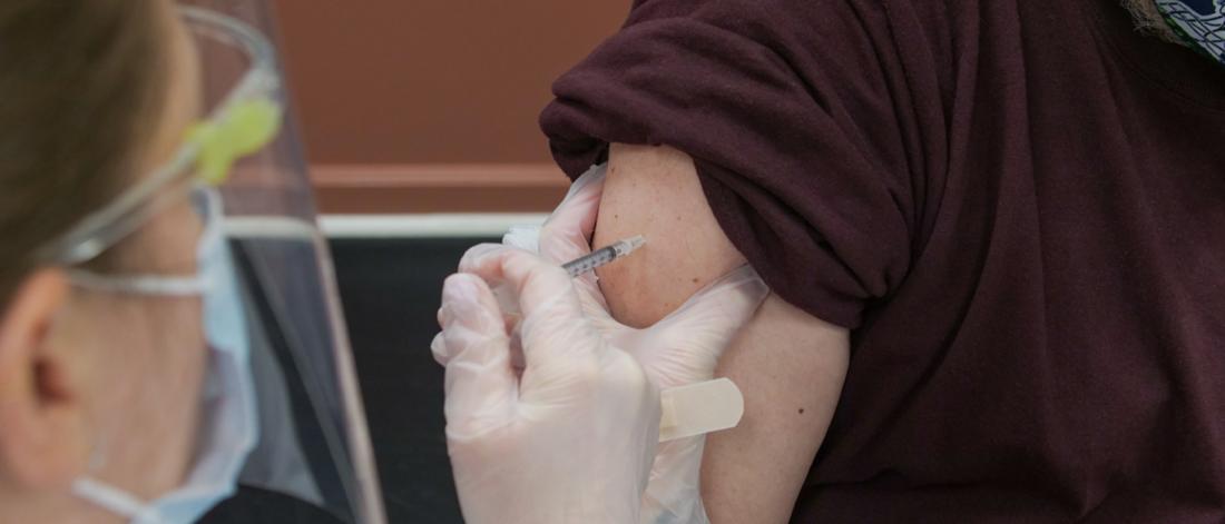 Masked and gloved nurse giving patient with rolled up sleeve Covid-19 vaccine