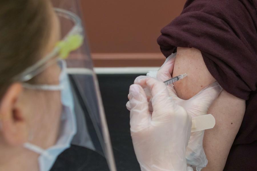 Masked nurse giving patient with rolled up sleeve covid 19 vaccine