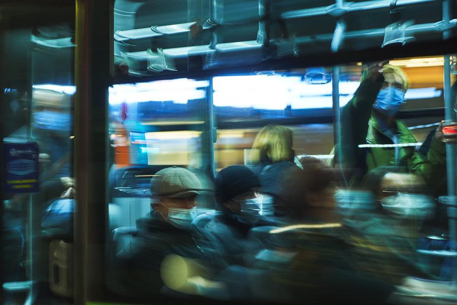 group of multicultural people sitting and standing on a city bus at night time