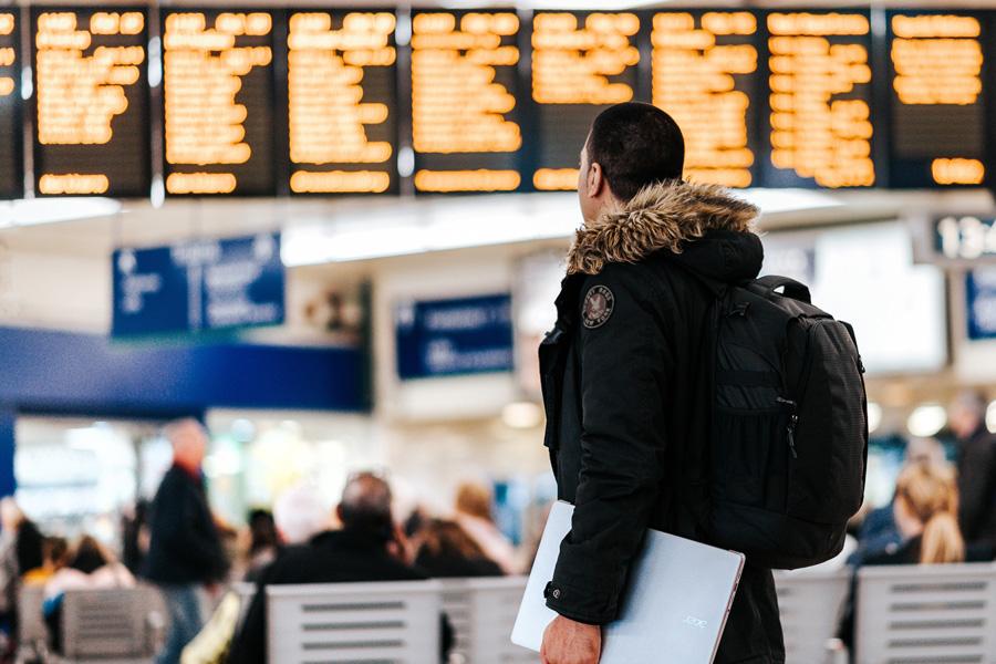 Man in wintercoat with backpack looking at arrivals/departures at airport
