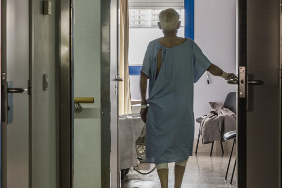 Back of Elderly man in hospital gown opening door to hospital room 