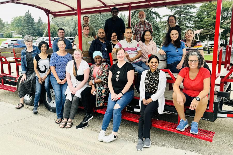 A large group of MCHP employees sitting on a large red wagon, smiling and waiting to go on a farm tour. 