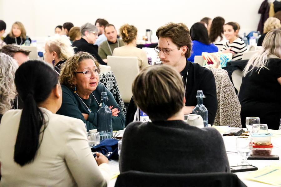 group of people at a banquet table listen intently to a colleague. 