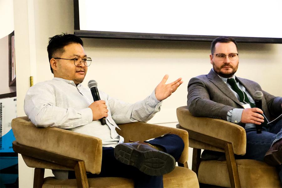 Lief Pagalan speaks with microphone in hand in panel discussion, while Tyler Amos listens 