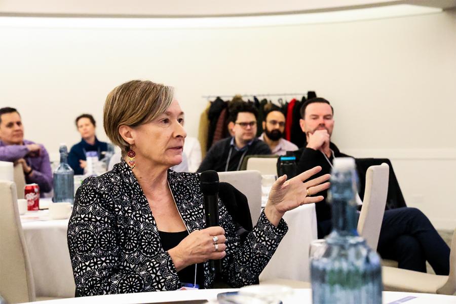 Dr. Josée Lavoie, mic in hand, seated at a banquet table, involved in discussion.