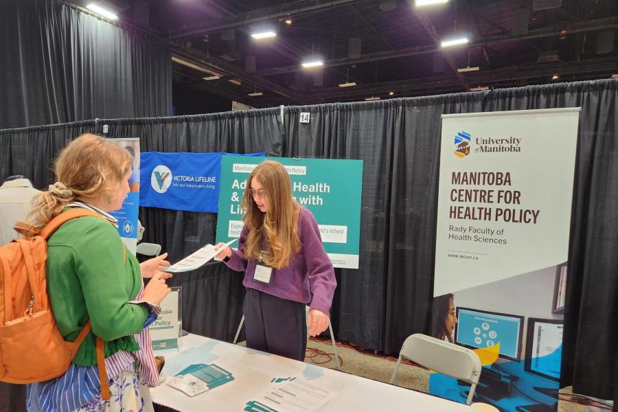 MCHP staff engage passer's by at a booth set up in a conference hall 
