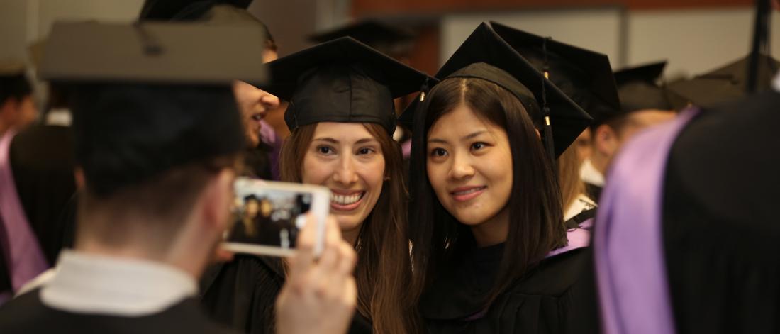 Two students dressed in graduation cap and gown posing for a photo.