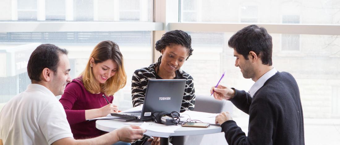 Four students seated together at a round table studying. 