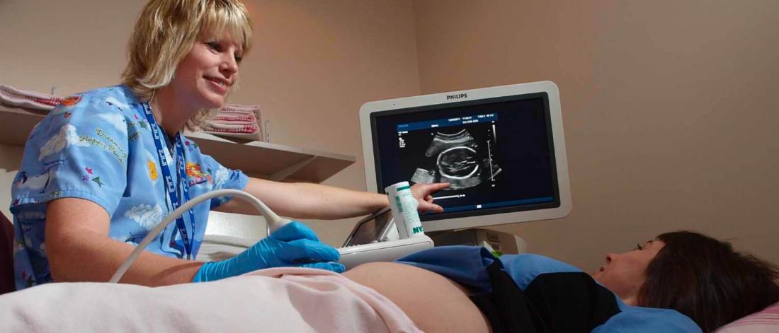 A medical professional points to a black and white monitor during an ultra-sound.
