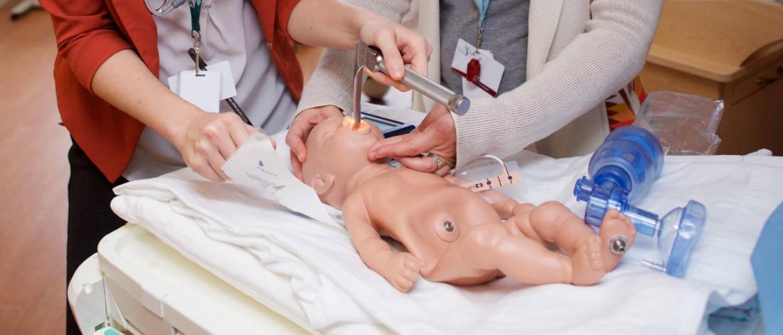 Two medical students practice skills using an infant simulation mannequin.
