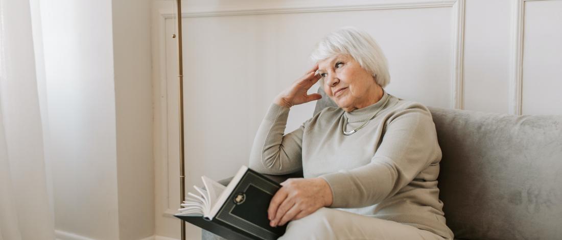 Senior holding a book and looking thoughtful.