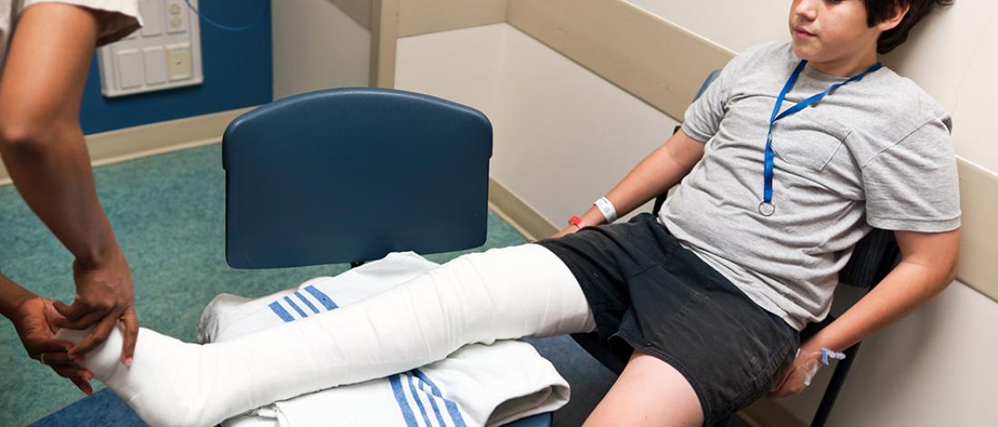 A child seated with their leg while their cast is being assessed. 