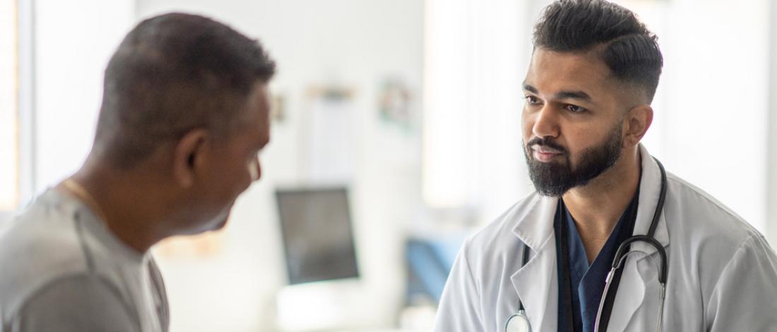 A male doctor takes notes during a medical appointment with a patient.