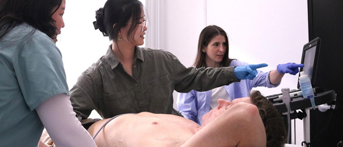 A preceptor and students practicing clinical skills on an acting patient.